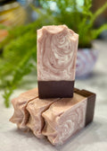 Swirled pink and brown natural soap on top of three soap bars lying down with a natural blurred background.