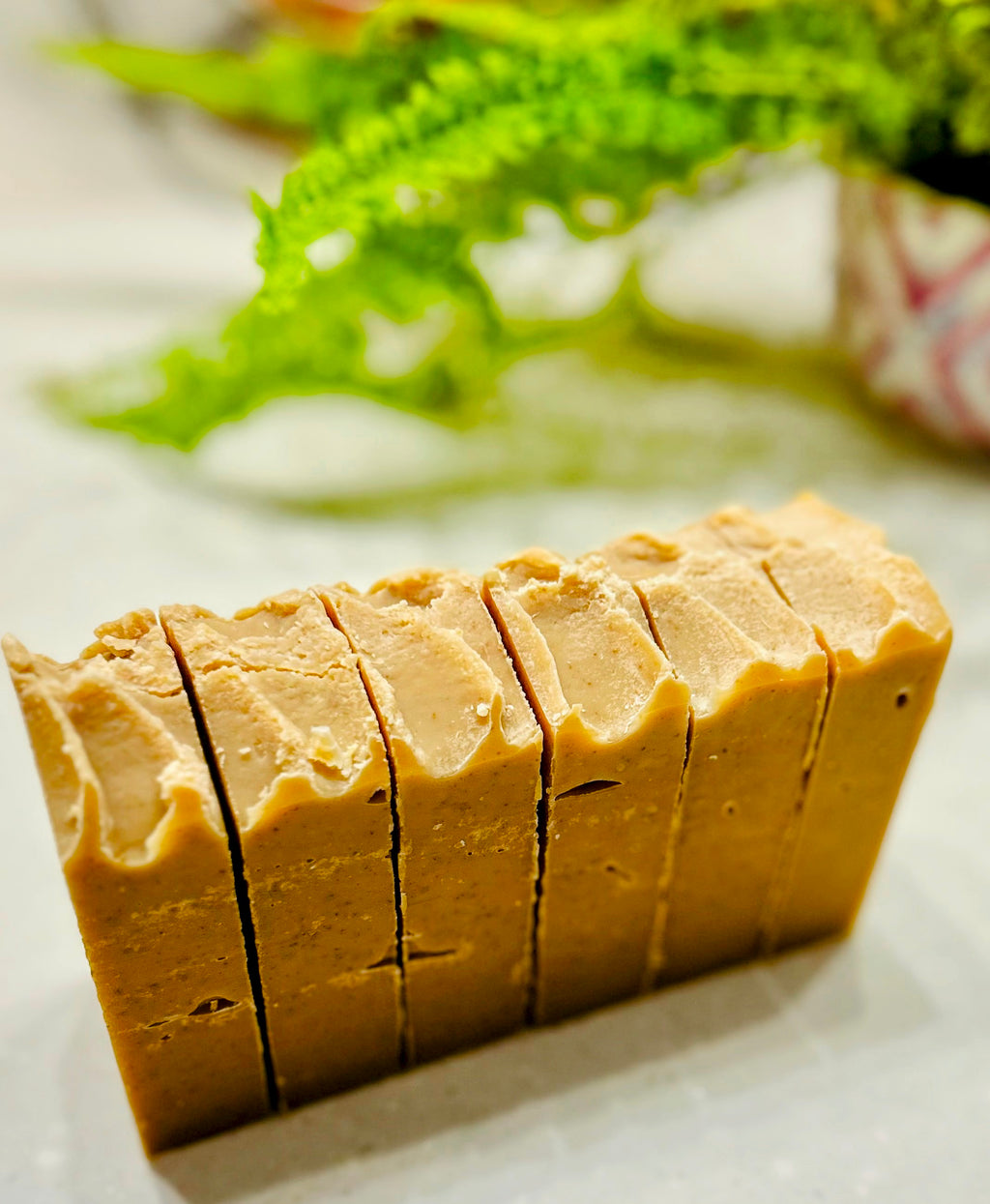 Block of sliced Gentle Bee natural soap on a white surface with greenery in the background