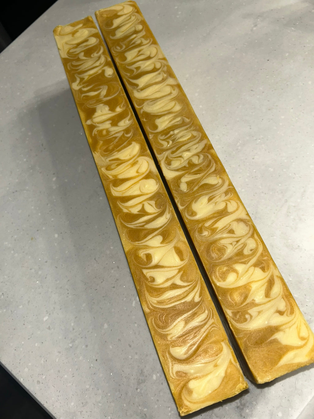 Two uncut loaves of yellow swirled soap on top of a white counter.