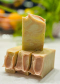 Three bars of handmade soap stacked on a white surface with a blurred natural background