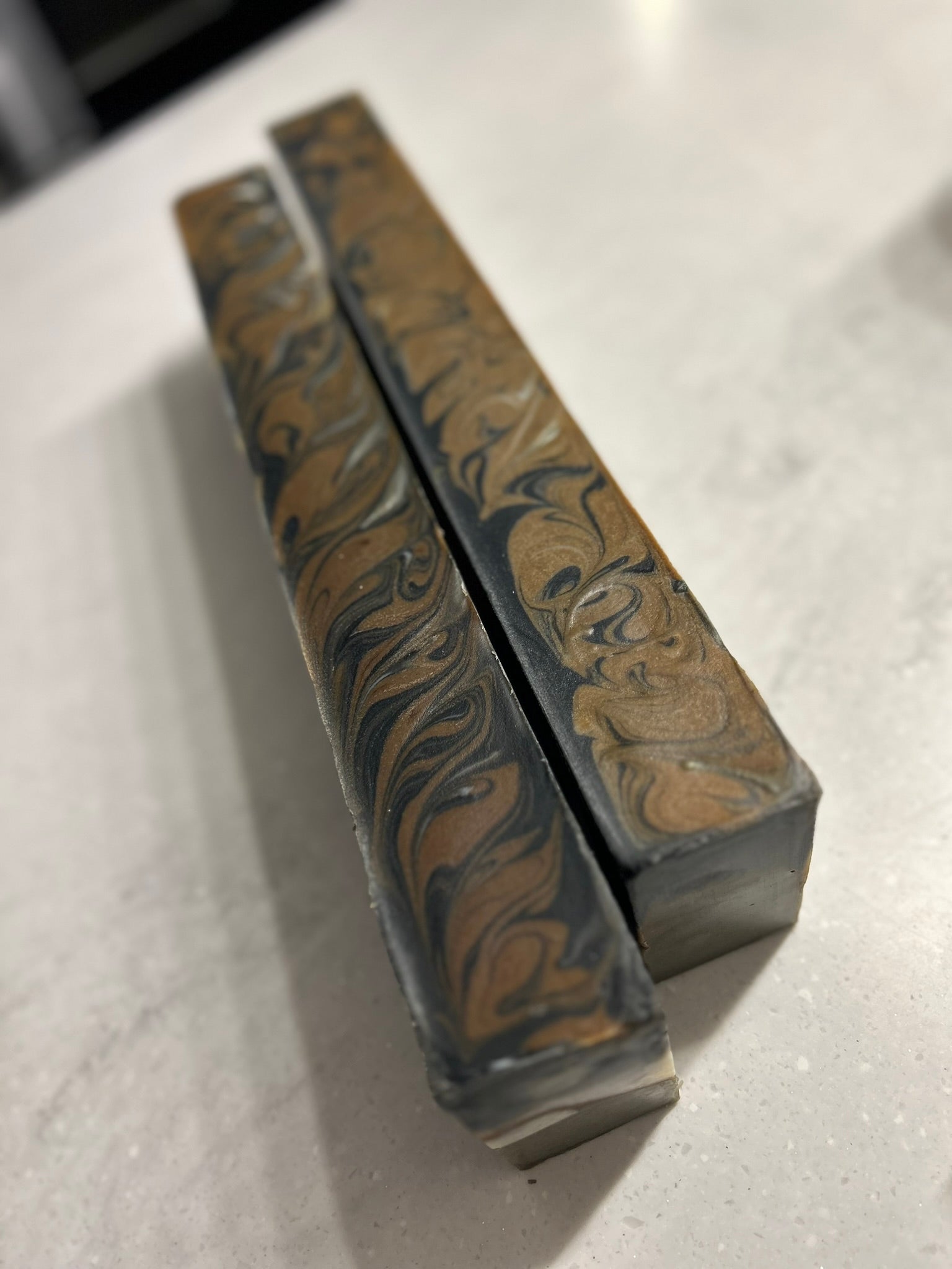 Two uncut loaves of natural handmade soap on top of a white counter top