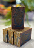 Handmade Tobacco Bay Leaf natural tallow soap, one bar standing upright facing forward, standing on top of three bars lying on their sides at an angle, with a blurred background.