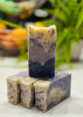 Stack of purple and white soap bars on a marble surface with blurred greenery in the background